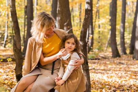 Young mother with her little daughter in an autumn park. Fall season, parenting and children concept.の写真素材