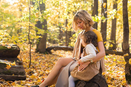 Young mother with her little daughter in an autumn park. Fall season, parenting and children concept.の写真素材