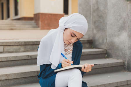 Female middle eastern college student sits on stairs in university campus. Education and knowledge concept.の写真素材