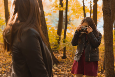 Child girl photographer takes pictures of a mother in the park in autumn. Hobbies, photo art and leisure concept.の写真素材