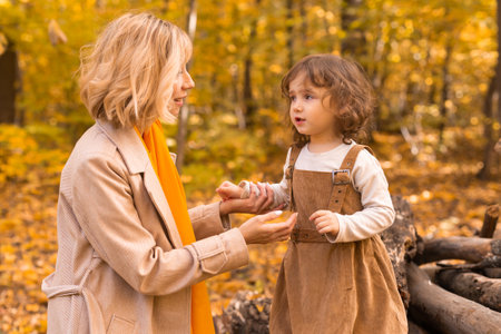 Young mother with her little daughter in an autumn park. Fall season, parenting and children concept.の写真素材