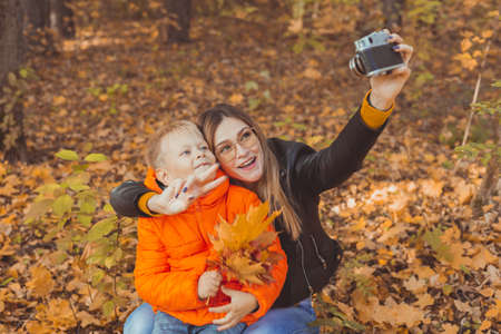 Son and mother are taking selfie on camera in autumn park. Single parent, leisure and fall season...