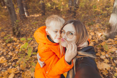 Son and mother are taking selfie and having fun in autumn park. Single parent, leisure and fall season concept.の写真素材