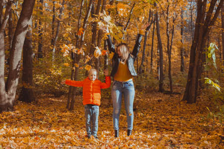 Single parent family playing with autumn leaves in park. Happy mom and son throw autumn leaves up in fall park.の写真素材