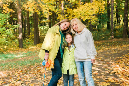 Portrait of three generations of happy beautiful woman looking at camera, hugging and smiling in autumn nature.の写真素材