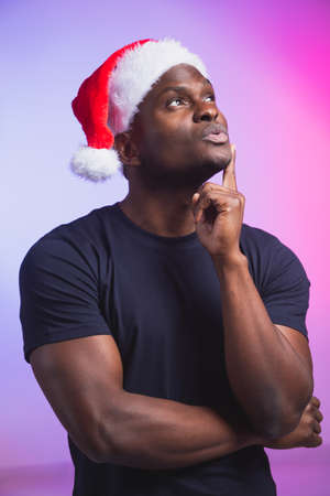 Portrait of pensive man in santa hat and casual t-shirt on colourful background, christmas time....