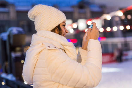 Happy young woman in winter on the ice rink taking picture on smartphone, selfie.の写真素材