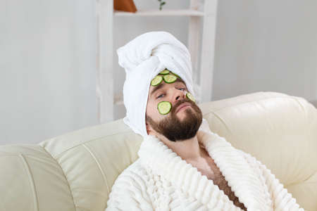 Bearded man holding cucumber slices on the face. Spa at home, body and skin care for male concept.の写真素材