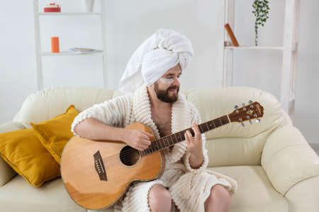 Young man with patches under the eyes plays on guitar at home. Concept of cosmetology for men and musican. Spa at home, music and skin careの写真素材