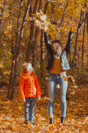 Single parent family playing with autumn leaves in park. Happy mom and son throw autumn leaves up in fall park.の写真素材