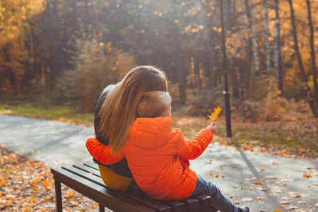 Single parent mother and child boy in the autumn in park sit on bench. Fall season and family concept.の写真素材