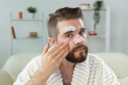 Bearded guy applying anti-wrinkle cream on his face. Skin care and spa for man concept.の写真素材