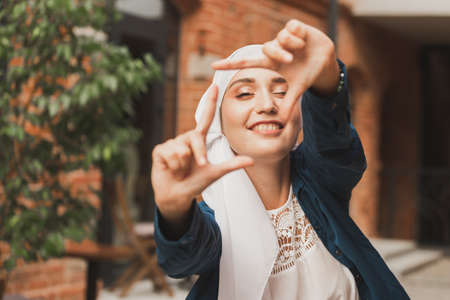 Portrait of young muslim girl making a camera frame with fingers outdoors.の写真素材