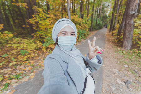 Muslim girl in a medical mask makes a selfie. Portrait of islamic arabian female student in park...