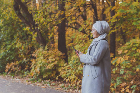 Muslim woman at the park using smartphone connected online wireless. Space for advertisementの写真素材