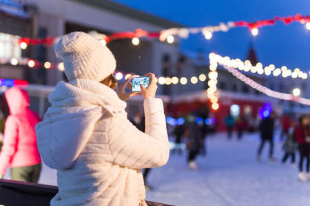 Happy young woman in winter on the ice rink taking picture on smartphone, selfie.の写真素材