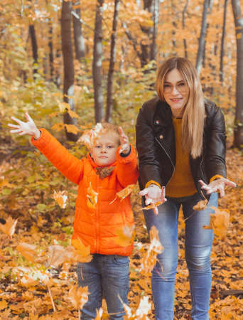 Single parent family playing with autumn leaves in park. Happy mom and son throw autumn leaves up in fall park.の写真素材