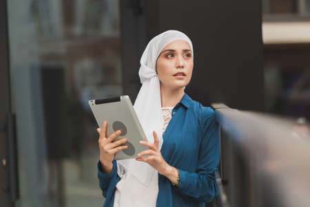 Beautiful Asian businesswomen wearing hijab using her tablet at outdoor.