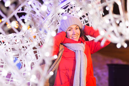 Winter holiday season. Christmas, New Year concept. Funny happy woman spend time having fun near illuminated and decorated showcase on city street.の写真素材