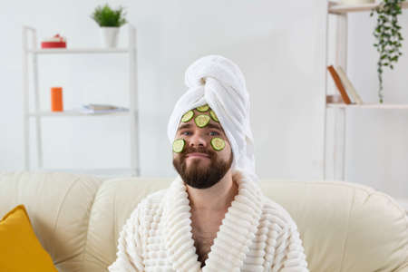 Bearded man holding cucumber slices on the face. Spa at home, body and skin care for male concept.の写真素材