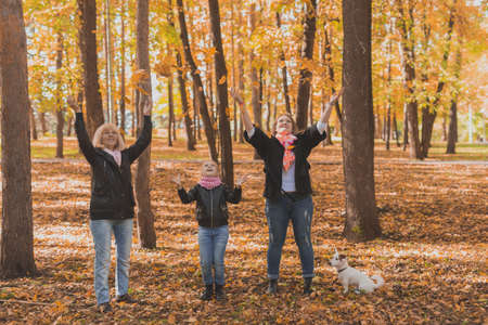 Grandmother and mother with granddaughter throw up fall leaves in autumn park and having fun. Generation, leisure and family concept.の写真素材