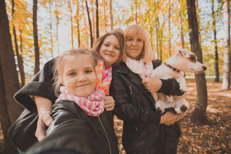 Mother, grandmother and little granddaughter with jack russell terrier dog taking selfie by smartphone outdoors in autumn nature. Family, pets and generation conceptの写真素材