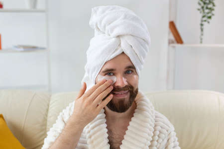 Young man with patches under the eyes at home. Concept of cosmetology for men. Spa at home, body and skin careの写真素材