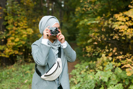 Young Arab Woman wearing hijab headscarf photographing with a smartphone in park. Modern muslim girl