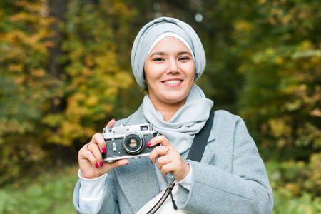 Young Arab Woman wearing hijab headscarf photographing with a smartphone in park. Modern muslim girlの写真素材