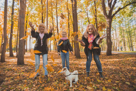 Grandmother and mother with granddaughter throw up fall leaves in autumn park and having fun....