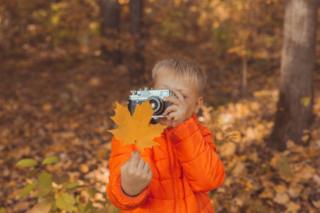 Boy with retro camera taking pictures outdoor in autumn nature. Leisure and photographers concept