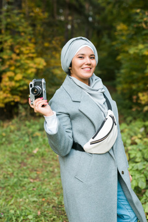 Young Arab Woman wearing hijab headscarf photographing with a smartphone in park. Modern muslim girlの写真素材