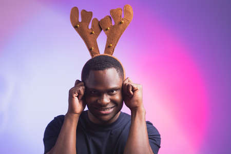 Portrait of emotional african american man wears rudolph deer horns enjoy his accessory for christmas eve party celebration on colourful backgroundの写真素材
