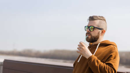 Stylish handsome hipster man holding drinks cocktail, spring time. Banner with copy space and place for advertisingの写真素材