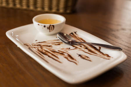 Empty dirty dish after cake with sauce and spoon. Messy plate on a table in cafeの写真素材