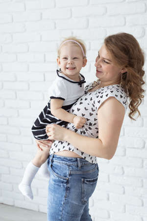 Mother holds her child with hearing aids and cochlear implants on white brick wall . Deaf and health conceptの写真素材