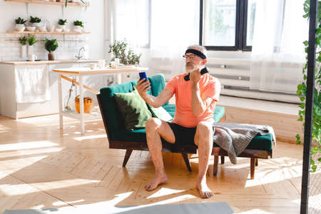 Elderly aged male taking selfie for social network during exercising with dumbbells. Old person man pensioner healthy training healthcare sport at home exercising fitness activity at elderly ageの写真素材