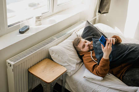 Freelance man using mobile phone checking social media network feed or message chat during lying on...
