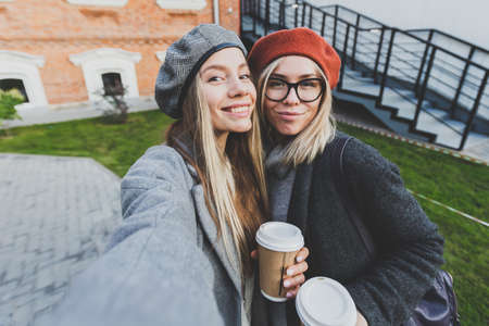 Two hipster girlfriends taking a self photo for social networks in urban city background -...
