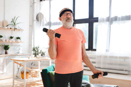 Elderly aged male exercising with dumbbells during online training. Old person man pensioner healthy...