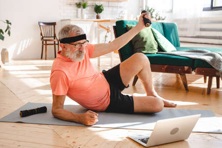 Senior man doing fitness exercises with virtual class and holding dumbbells - wellbeing and wellness conceptの写真素材