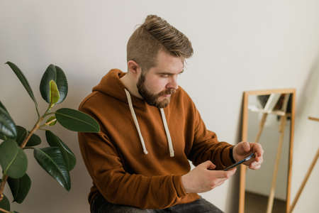 Freelance man using mobile phone checking social media network feed or message chat at home. Online digital communication and rest after hard work dayの写真素材