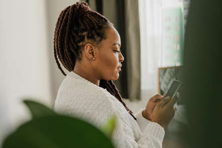 Portrait of African American female student dressed casually holding mobile phone and typing messages and communicating with friends via social networks using high-Internet connection.の写真素材