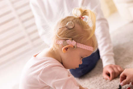 Baby with cochlear implants having fun at home. Deafness and medical technology concept.の写真素材