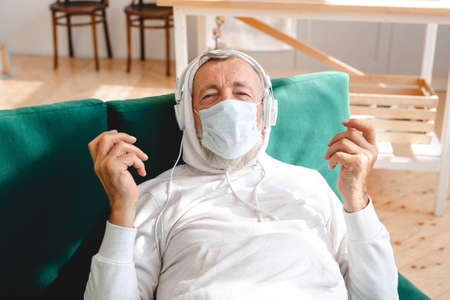Senior man with medical mask on face using smartphone app for creating playlist music - Elderly male...