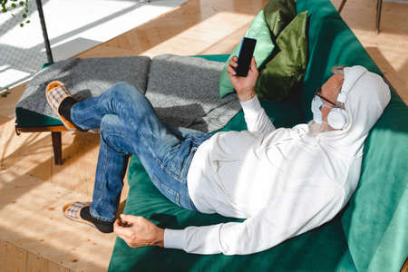 Senior man with medical mask on face using smartphone app for creating playlist music - Elderly male...