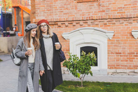 Two girls walking on street together and holding their hands. They are wearing spring or autumn...