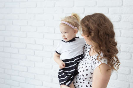 Mother holds her child with hearing aids and cochlear implants on white brick wall with copy space and place for advertising . Deaf and health conceptの写真素材