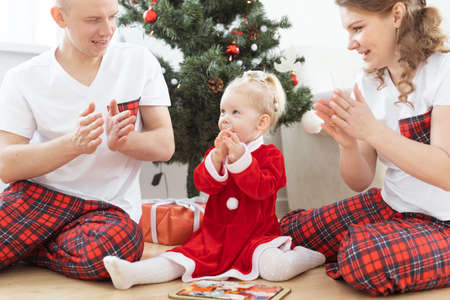 Toddler child with cochlear implant plays with parents under christmas tree - deafness and...