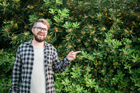 Close up portrait handsome young man point over green bush outside copy space and place for...